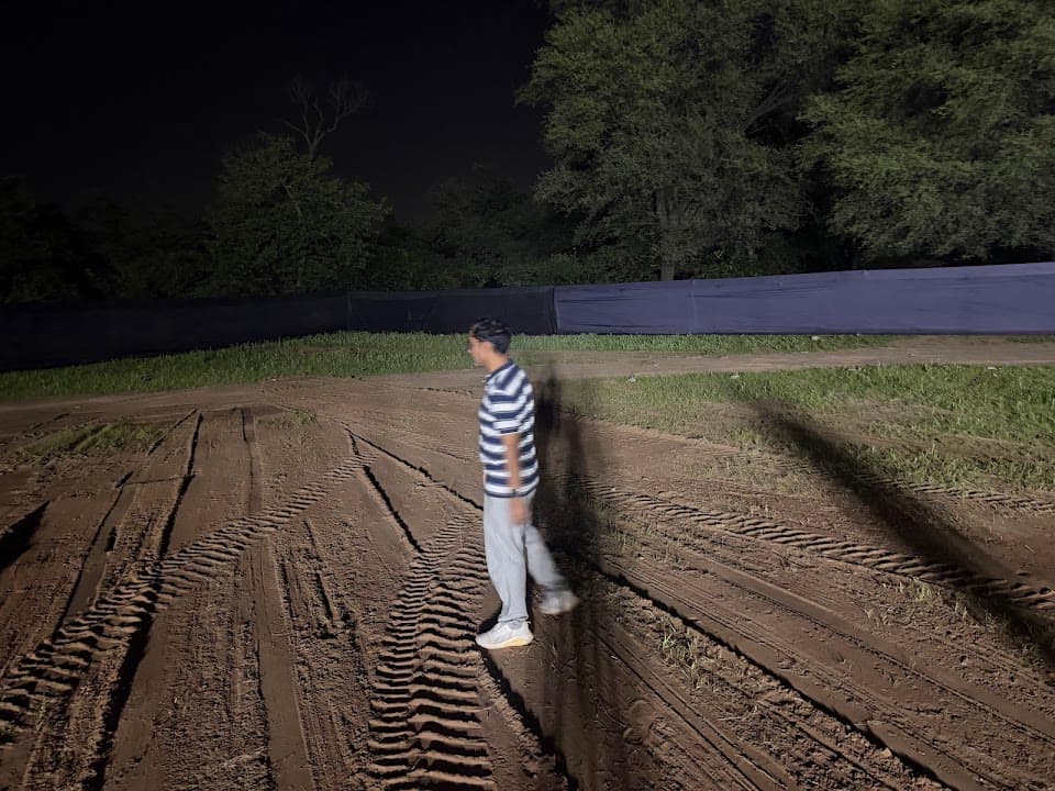 Airoveda team member inspecting the muddy drone launch area at Bhagwat Katha Ground in Gandhinagar at 8:40 PM on 9 August 2026